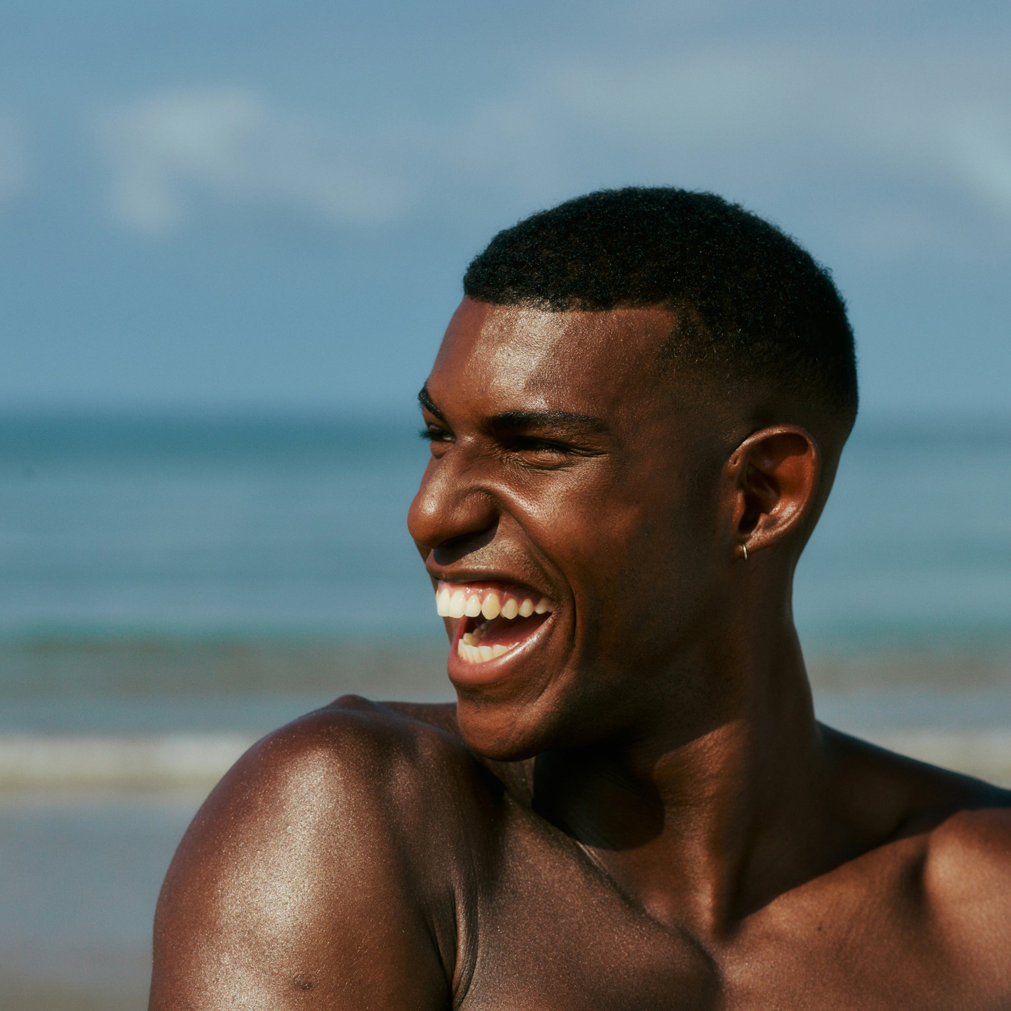Man laughing on a beach with clear blue sky and ocean in the background