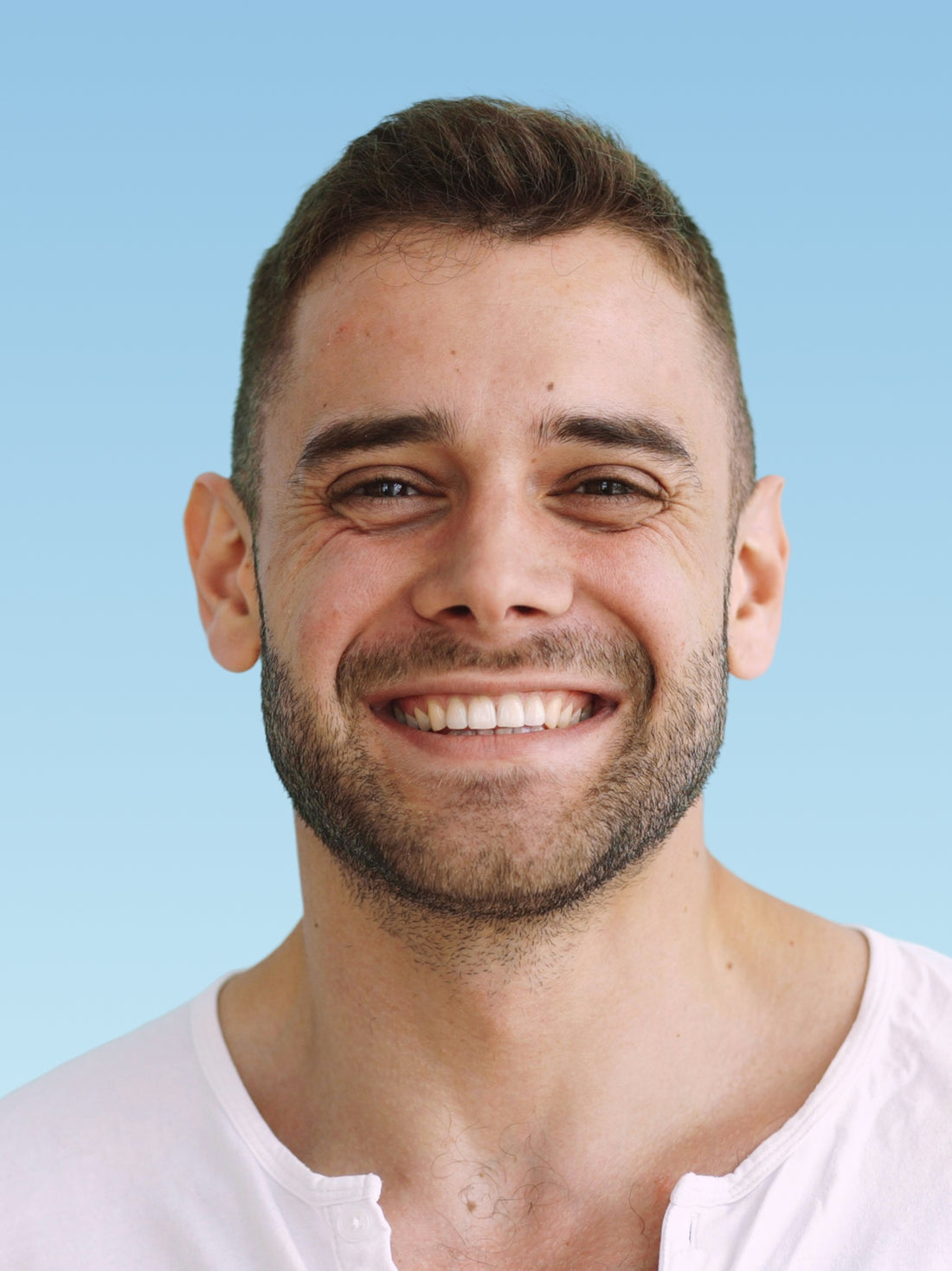 Man with a beard and short hair smiling against a light blue background