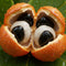 Close-up of a split fruit revealing black and white seeds on a green leaf background