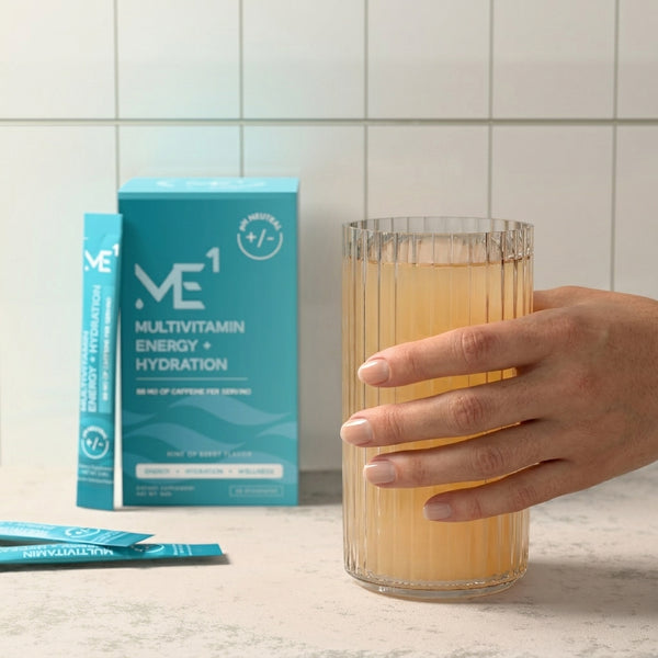 Glass of orange juice with a ME1 multivitamin energy hydration box on a tiled countertop.