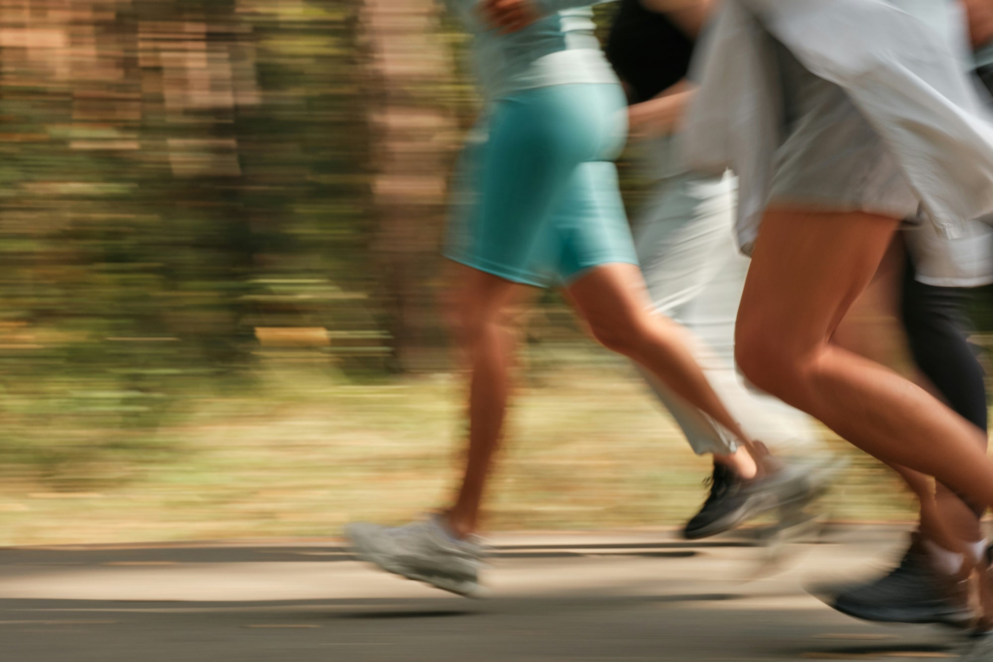 Blurred image of people running on a road with greenery in the background